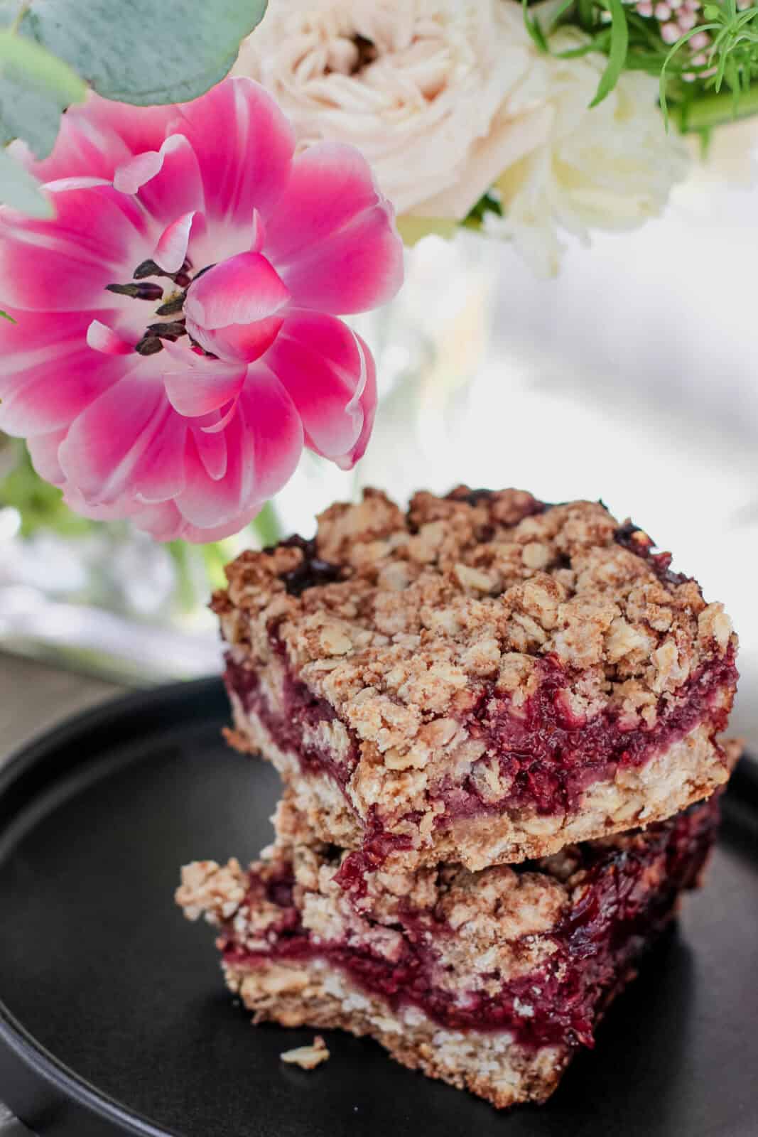 A plate of gluten-free berry crumble bars on a table with flowers.