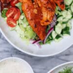 Buffalo chicken salad with homemade ranch dressing, crisp lettuce, cucumbers, cherry tomatoes, red onion, and bacon in a white bowl on a marble surface.