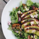 Overhead view of grilled chicken salad with basil vinaigrette, goat cheese, pecans, and summer peaches on a bed of romaine lettuce.