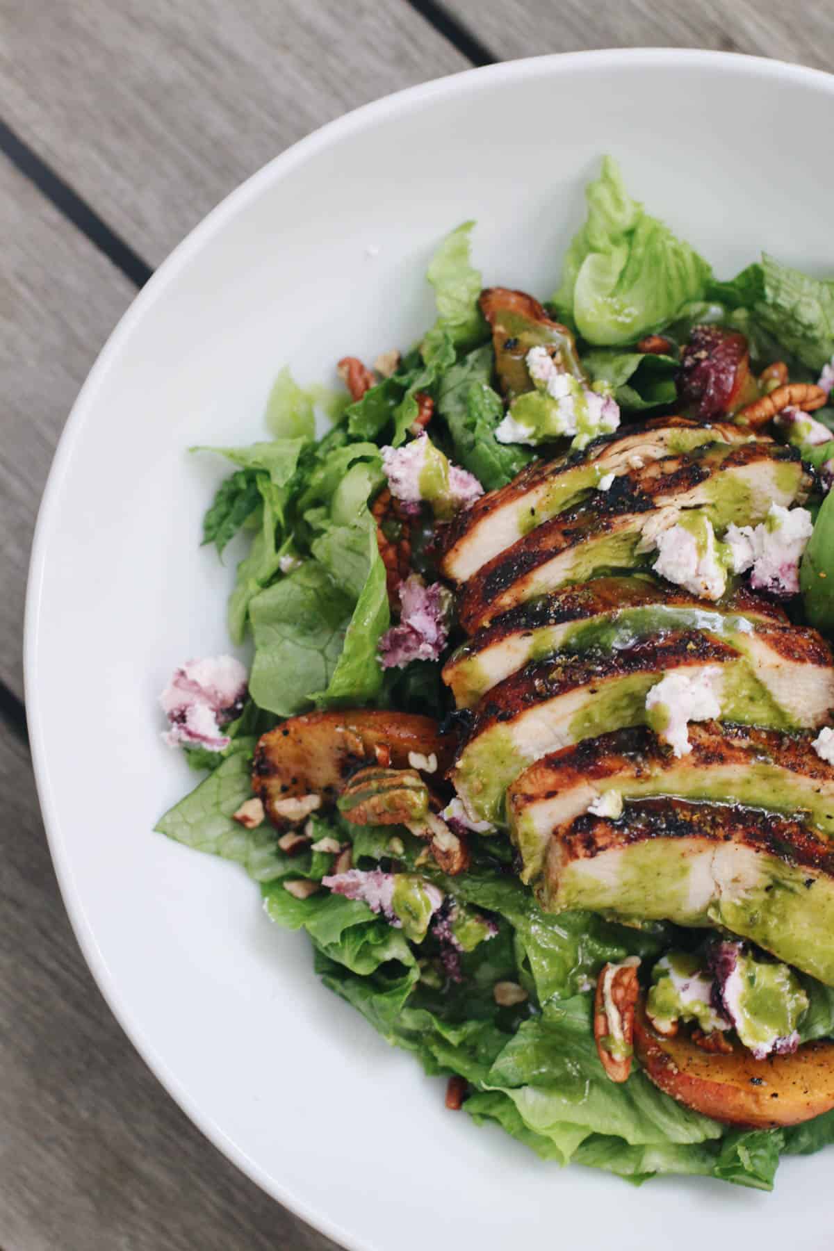 Overhead view of grilled chicken salad with basil vinaigrette, goat cheese, pecans, and summer peaches on a bed of romaine lettuce.