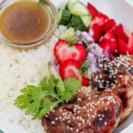 Overhead image of a summer strawberry salad bowl with balsamic chicken, sliced strawberries, cucumbers, red onion, and rice, drizzled with vinaigrette in a white bowl.