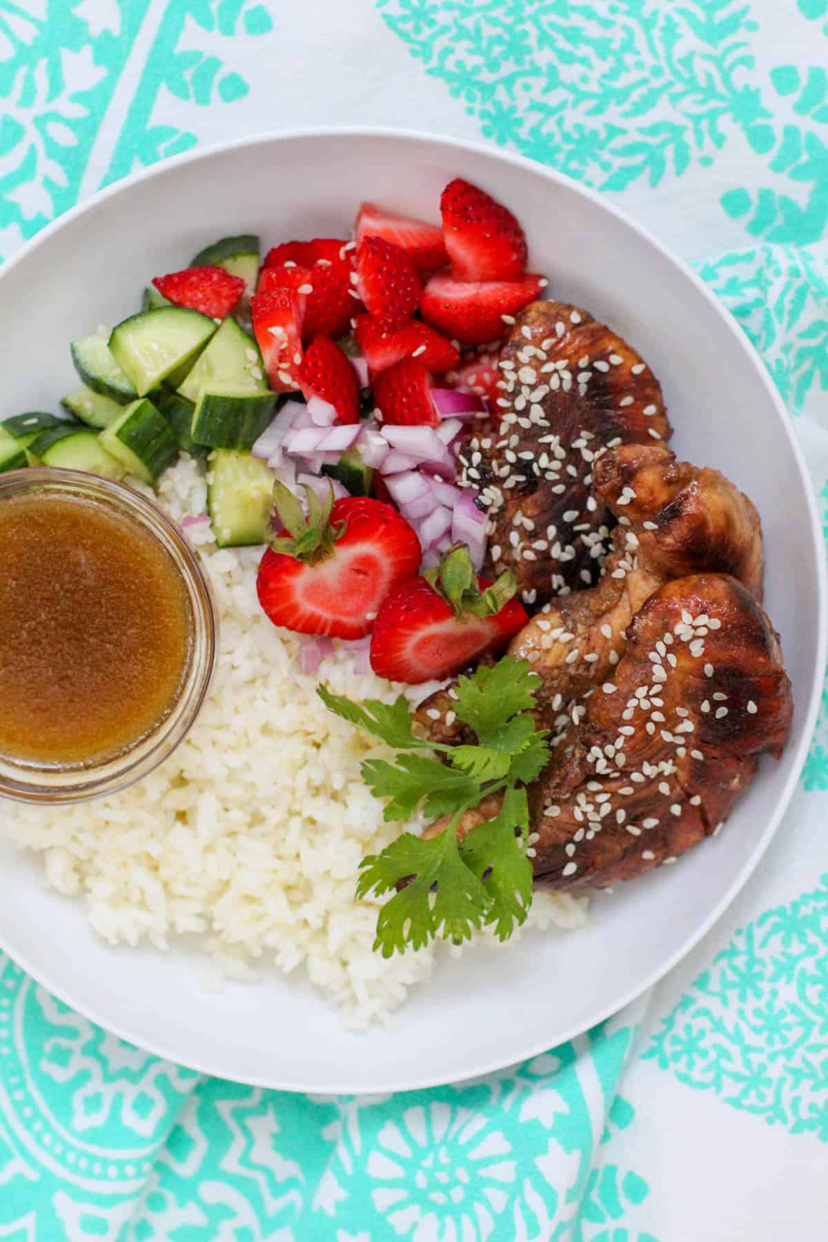 Overhead image of a summer strawberry salad bowl with balsamic chicken, sliced strawberries, cucumbers, red onion, and rice, drizzled with vinaigrette in a white bowl.