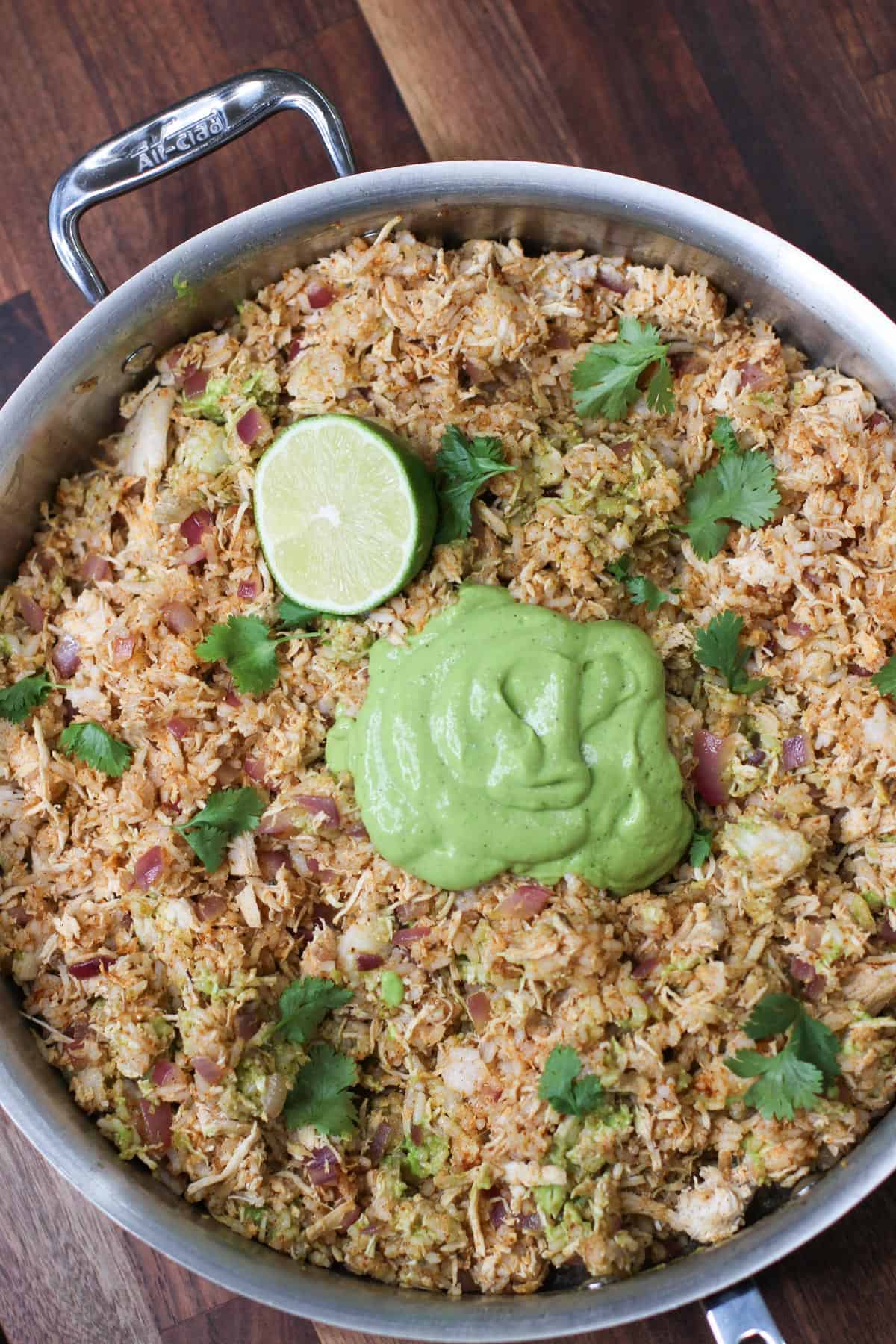 One-pan arroz con pollo topped with vibrant avocado cilantro lime crema, garnished with fresh cilantro and lime. A flavorful, dairy-free and gluten-free chicken and rice dinner perfect for meal prep or casual hosting