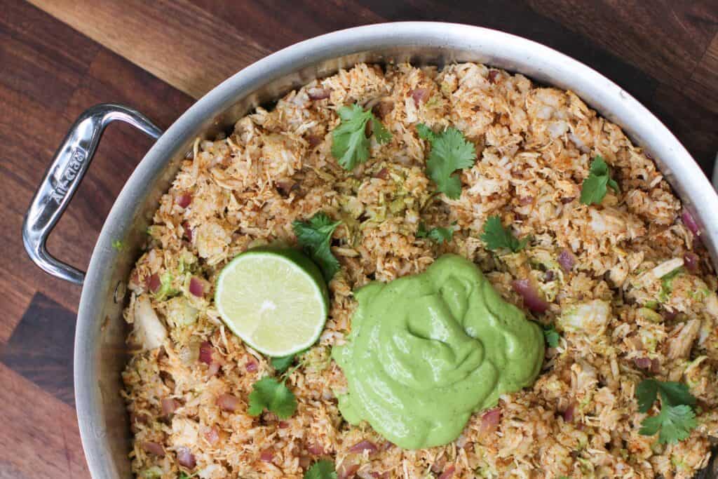 One-pan arroz con pollo topped with vibrant avocado cilantro lime crema, garnished with fresh cilantro and lime. A flavorful, dairy-free and gluten-free chicken and rice dinner perfect for meal prep or casual hosting