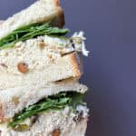 Close-up of a stacked chicken salad sandwich on thick bread with leafy greens, showing a creamy chicken filling mixed with pistachios.