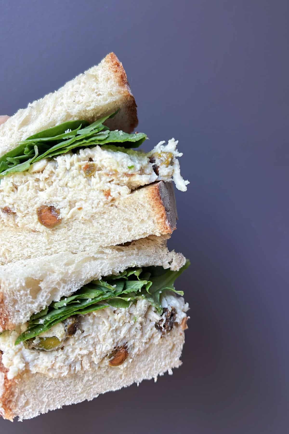 Close-up of a stacked chicken salad sandwich on thick bread with leafy greens, showing a creamy chicken filling mixed with pistachios.