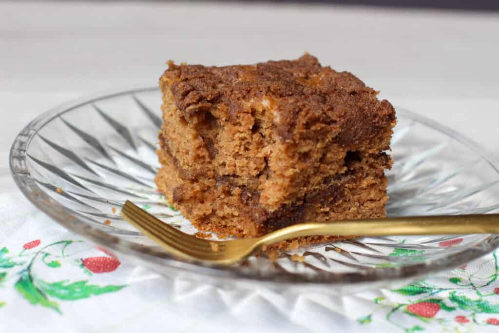 A golden slice of gluten-free cinnamon streusel coffee cake on a plate, topped with crumbly coconut sugar streusel and served with a cup of coffee. Ideal for brunch or a cozy weekend bake.