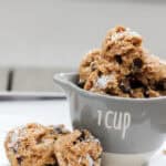 Close-up of coconut chocolate chip protein bites stacked in a 1-cup measuring cup, topped with shredded coconut and chocolate chips, on a white tray.