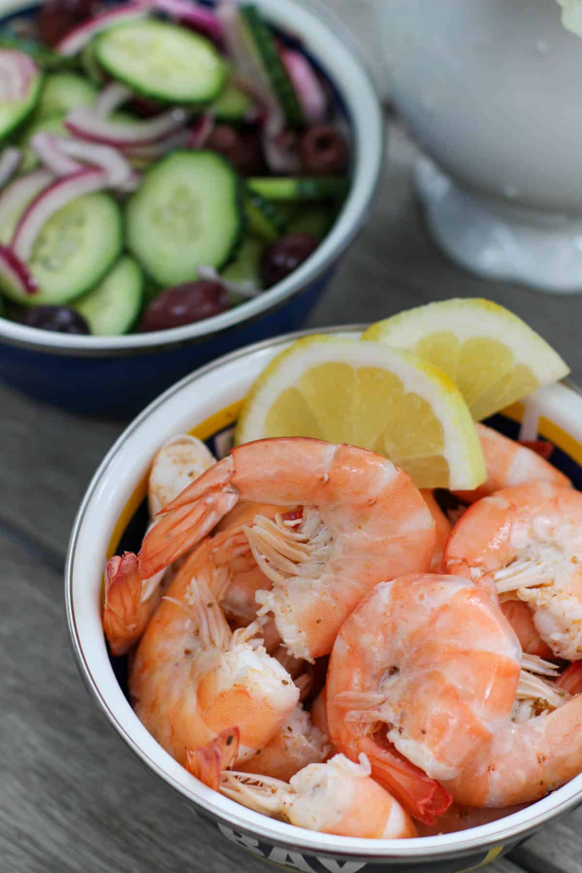 Fresh shrimp with lemon wedges and side salad of cucumbers, onions, olives, and radishes, healthy seafood meal, fit to entertain.