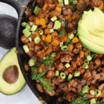 Overhead view of Texas sweet potato skillet in cast iron pan, topped with avocado and green onion.