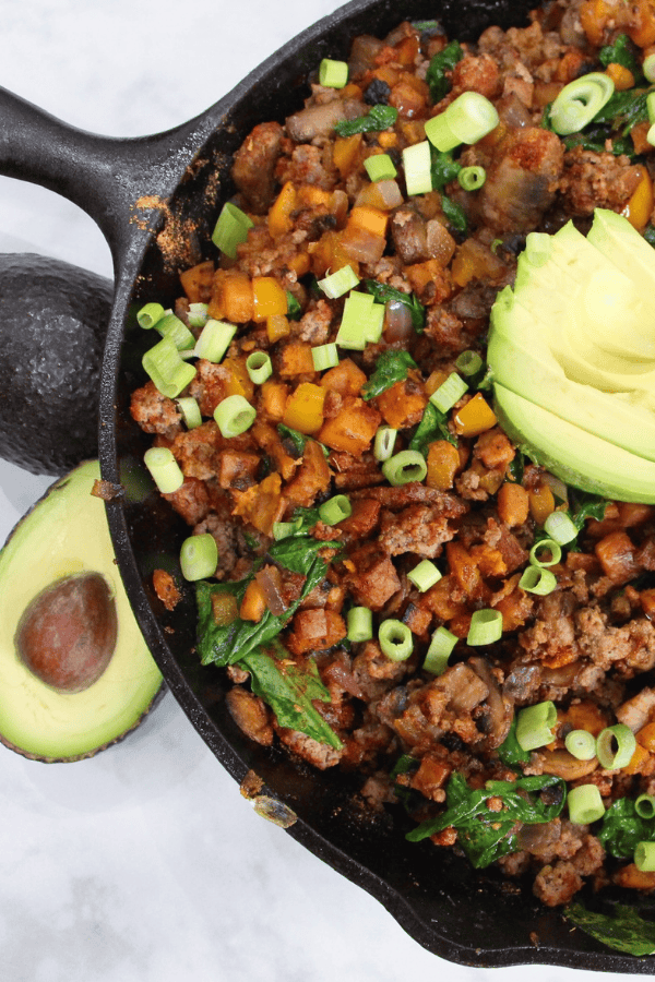 Overhead view of Texas sweet potato skillet in cast iron pan, topped with avocado and green onion.