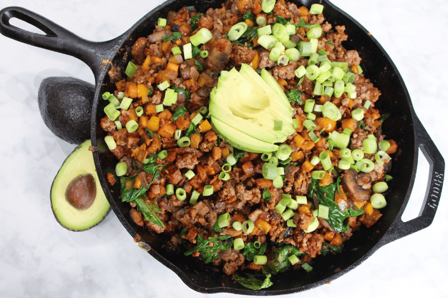 Overhead view of Texas sweet potato skillet in cast iron pan, topped with avocado and green onion.