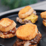 Pulled pork sliders on roasted sweet potato rounds, drizzled with barbecue sauce and served on a party platter.