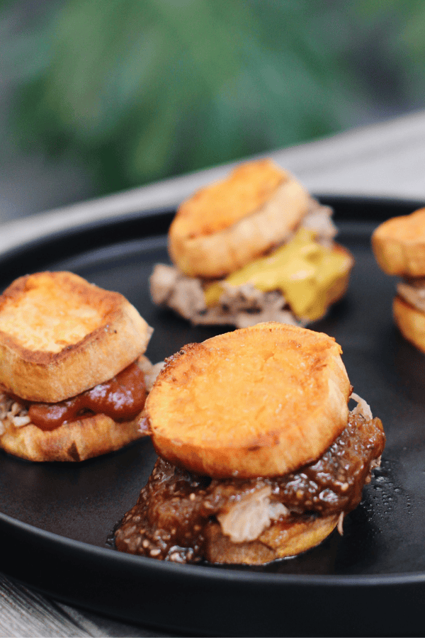 Pulled pork sliders on roasted sweet potato rounds, drizzled with barbecue sauce and served on a party platter.