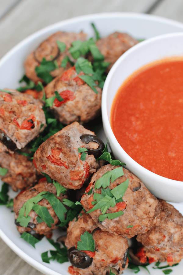 Plate of pizza burger bites with marinara dipping sauce, garnished with fresh parsley.