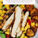 Cuban-inspired salad with grilled chicken, crispy golden plantain “croutons”, and pineapple mango salsa over a bed of lettuce and red cabbage, served in a white bowl on a marble background.