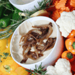 A creamy gluten- and dairy-free French onion dip made from cashews, topped with caramelized onions and surrounded by colorful crudité.