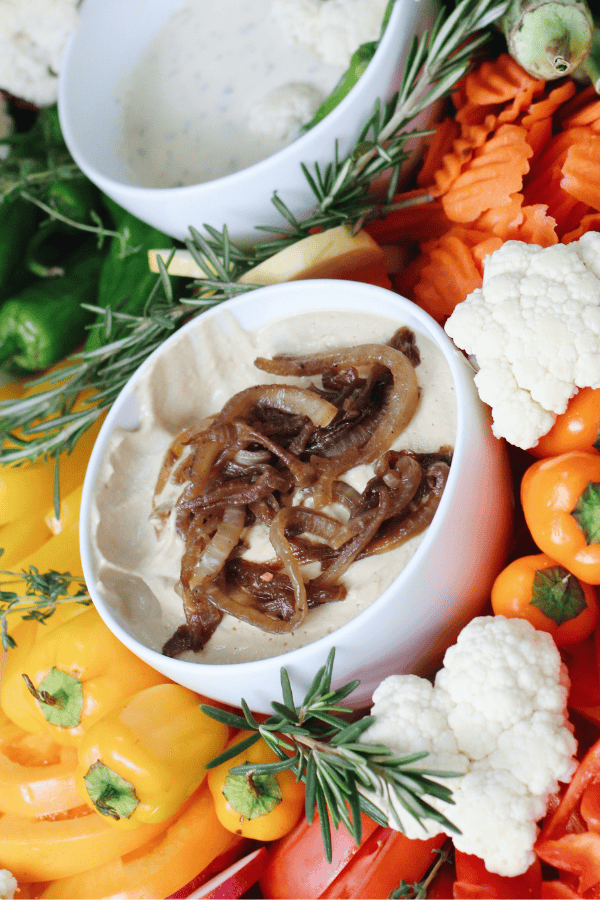 A creamy gluten- and dairy-free French onion dip made from cashews, topped with caramelized onions and surrounded by colorful crudité.