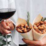 Two cones of rosemary cocktail nut mix held next to a glass of wine—perfect for easy entertaining.