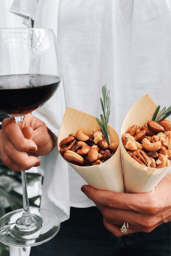 Two cones of rosemary cocktail nut mix held next to a glass of wine—perfect for easy entertaining.