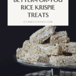 Rice Krispies treats cut into squares arranged on a glass cake stand with a fall linen napkin under it.