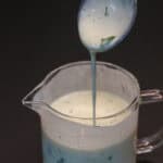 Herbed buttermilk ranch being poured from a spoon into a glass measuring cup.