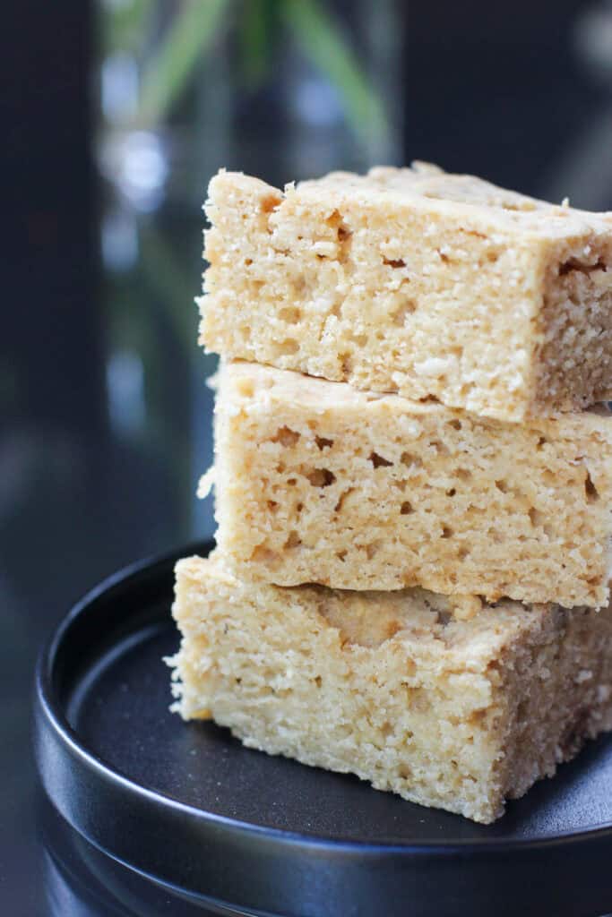 A stack of three pieces of homemade cornbread cut into squares, sitting on a round black plate.