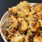 Crispy baked chicken bites in a white bowl on black background.