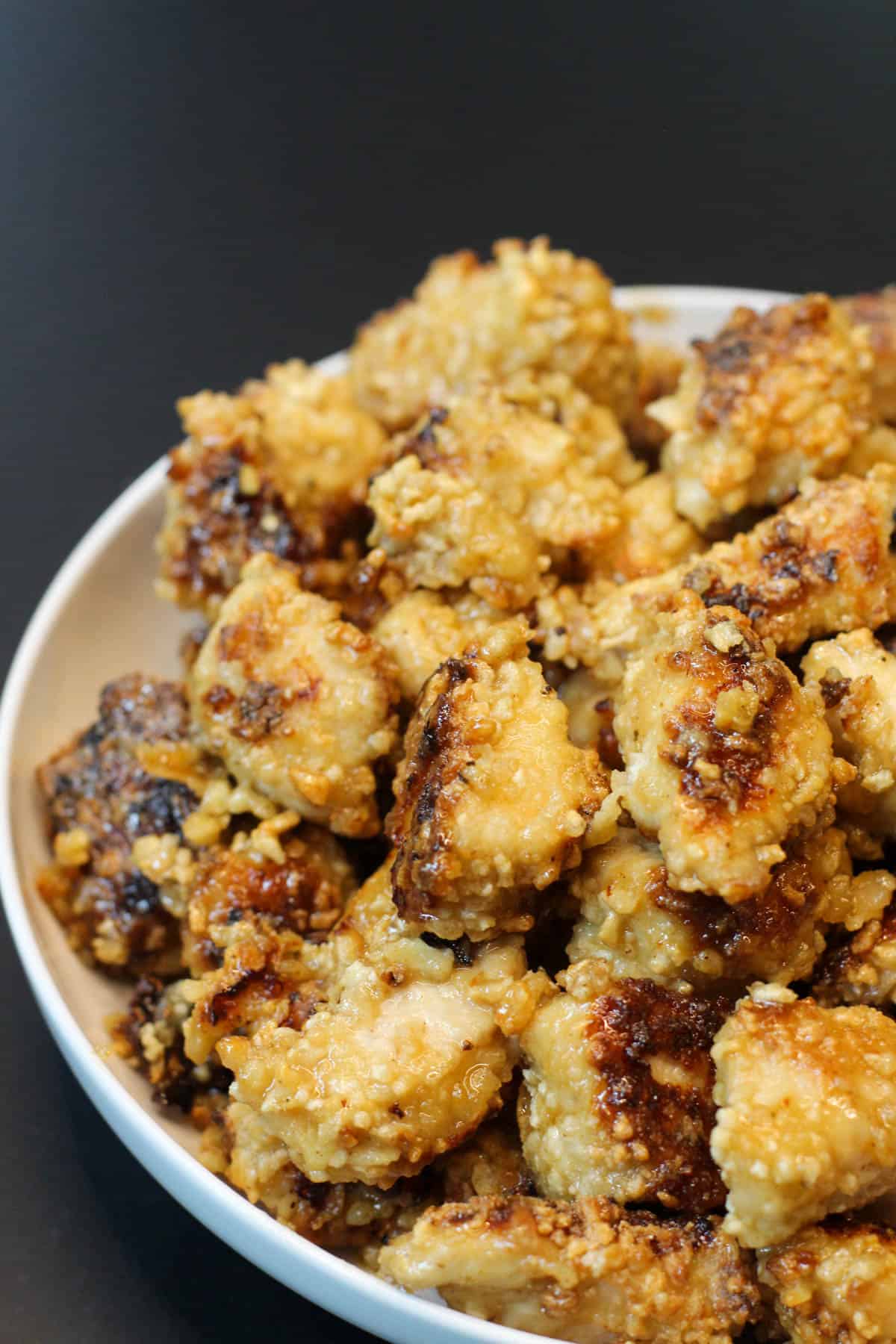 Crispy baked chicken bites in a white bowl on black background.