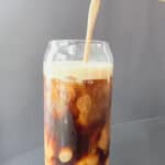 A clear glass of iced coffee topped with homemade salted pumpkin coffee creamer. The creamy foam swirls into the coffee, dusted with pumpkin pie spice and a pinch of flaky Redmond Real Salt, creating a cozy fall drink that looks rich, smooth, and inviting.