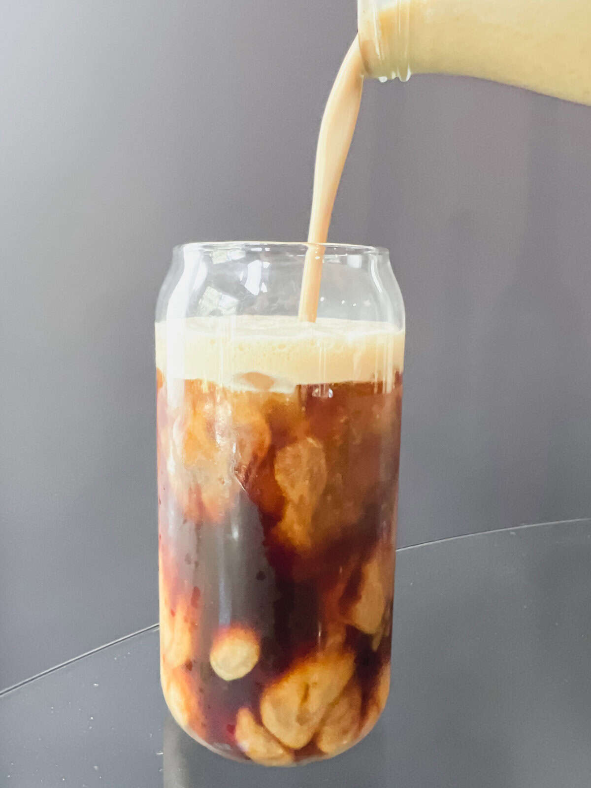 A clear glass of iced coffee topped with homemade salted pumpkin coffee creamer. The creamy foam swirls into the coffee, dusted with pumpkin pie spice and a pinch of flaky Redmond Real Salt, creating a cozy fall drink that looks rich, smooth, and inviting.