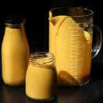 Creamy mango smoothie in glass bottles and measuring jug.