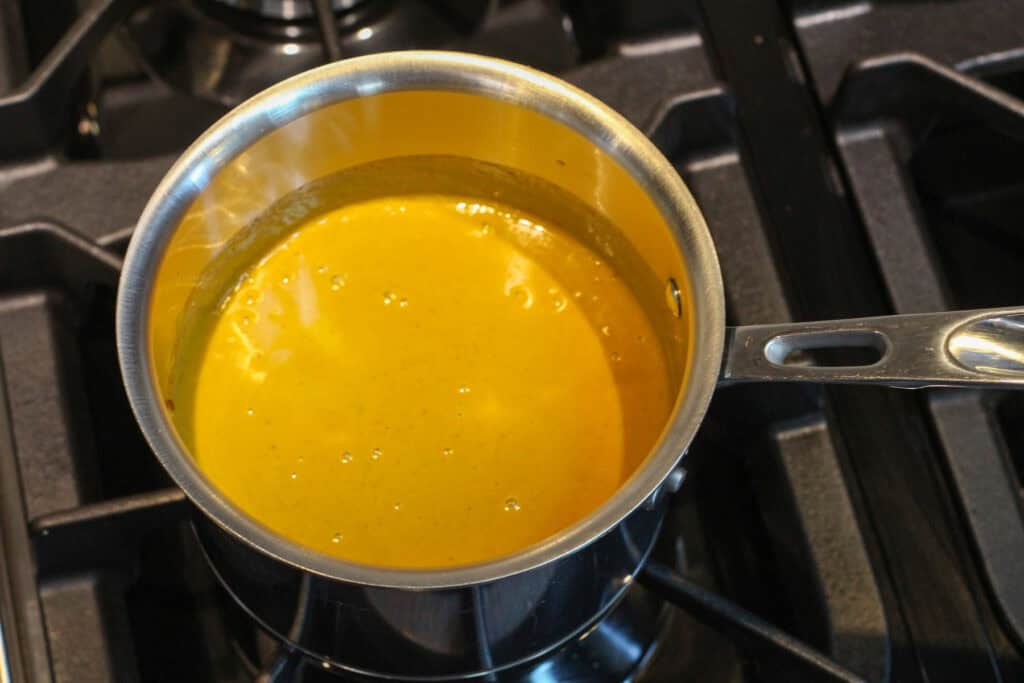 Creamy butternut squash soup in a silver saucepan on a stovetop.