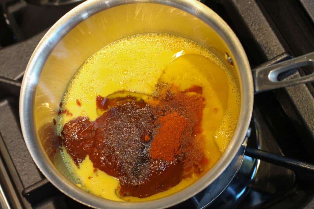 Creamy Carolina Gold BBQ Sauce is in three glass jars. Some sauce drips down the side of one jar. They are all on a black countertop.