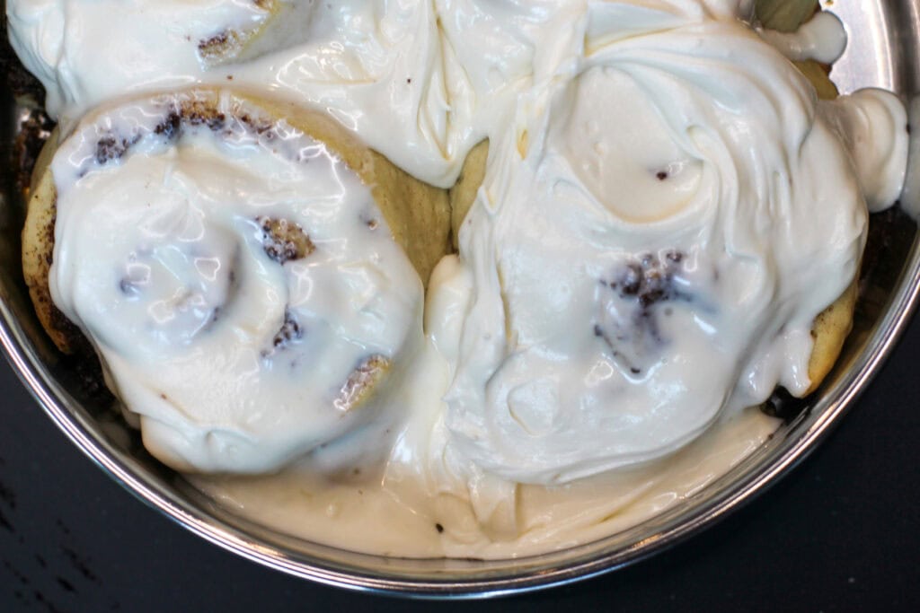 Cream cheese cinnamon rolls with icing in a metal baking dish.