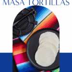 Freshly pressed homemade masa tortillas on a black plate beside a traditional cast-iron tortilla press and colorful striped cloth, ready for cooking or serving.