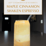 A glass of maple cinnamon shaken espresso with frothy layers and a glass straw, sitting on a dark countertop in natural light.