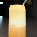 A glass of maple cinnamon shaken espresso with frothy layers and a glass straw, sitting on a dark countertop in natural light.