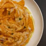 A close-up of creamy sweet potato mash swirled with whipped ricotta and drizzled with maple syrup, topped with fresh thyme leaves for an elegant, cozy presentation.