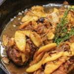 Cider-braised pork loin topped with caramelized apple-onion compote and fresh thyme in a cast iron skillet.