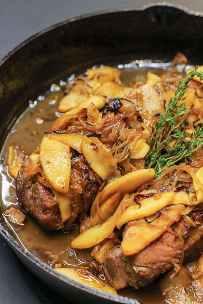 Cider-braised pork loin topped with caramelized apple-onion compote and fresh thyme in a cast iron skillet.