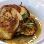 Plate of crispy-skinned chicken thighs served with rosemary jus and pan-seared polenta cakes on a white dish.