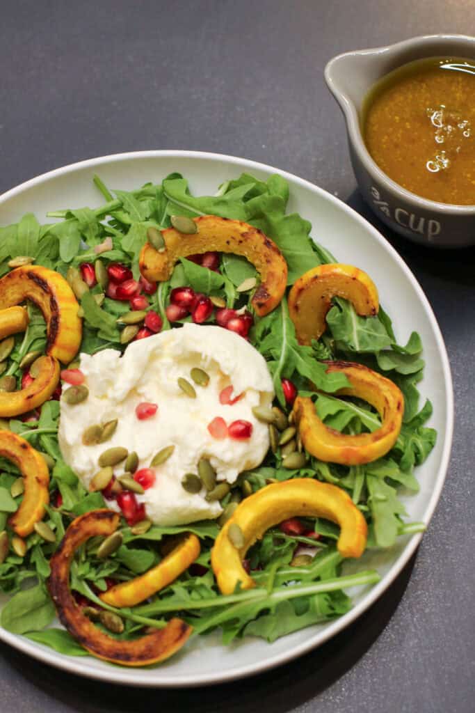 A vibrant roasted delicata squash and burrata salad topped with pomegranate seeds and pumpkin seeds, drizzled with maple-cider vinaigrette.