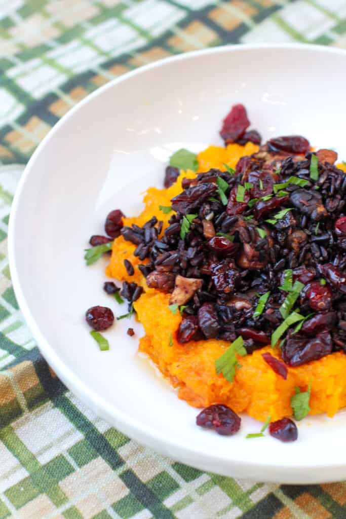 Roasted honeynut squash halves filled with wild rice, mushrooms, cranberries, and toasted pecans, garnished with fresh parsley on a white plate.