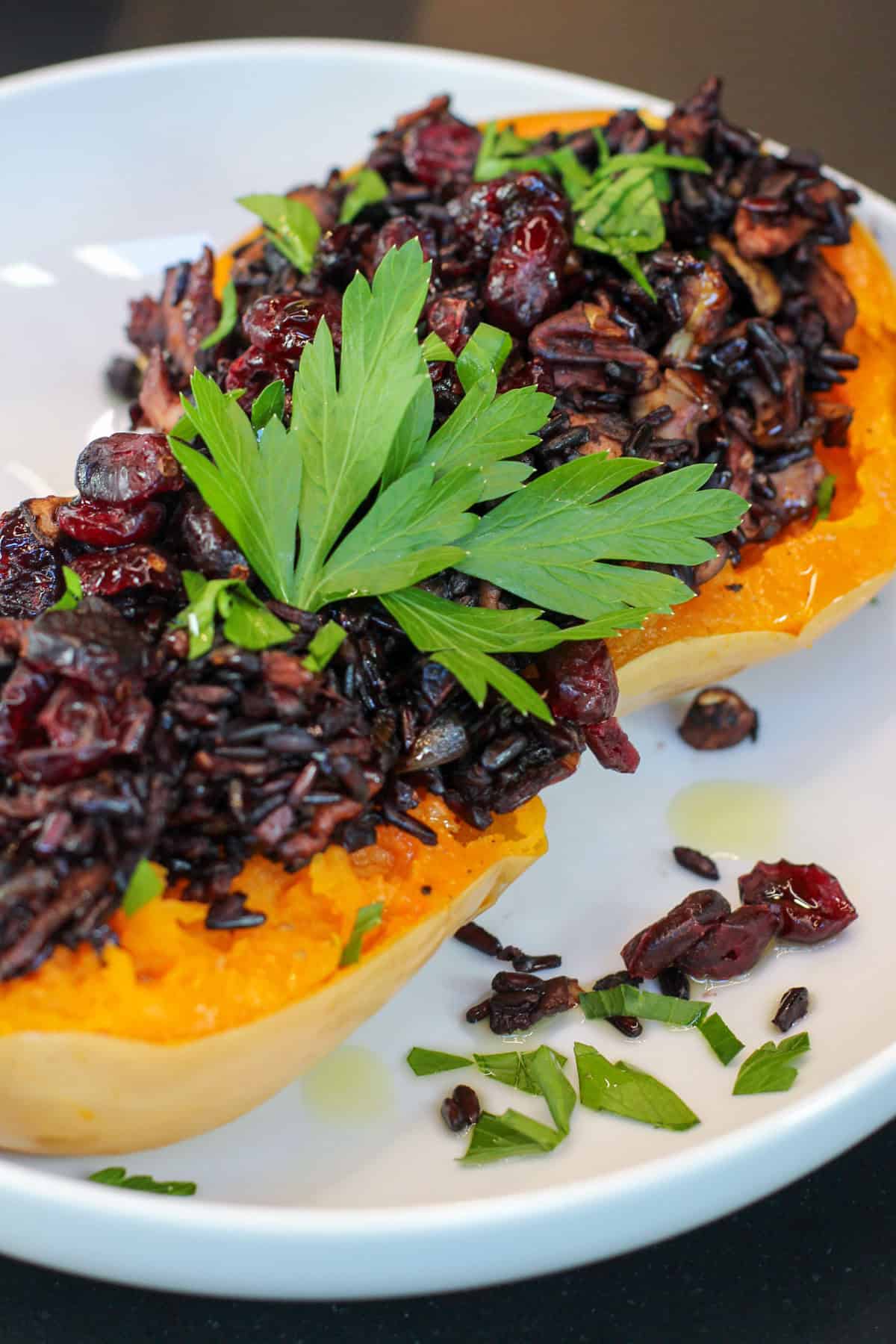 Roasted honeynut squash halves filled with wild rice, mushrooms, cranberries, and toasted pecans, garnished with fresh parsley on a white plate.