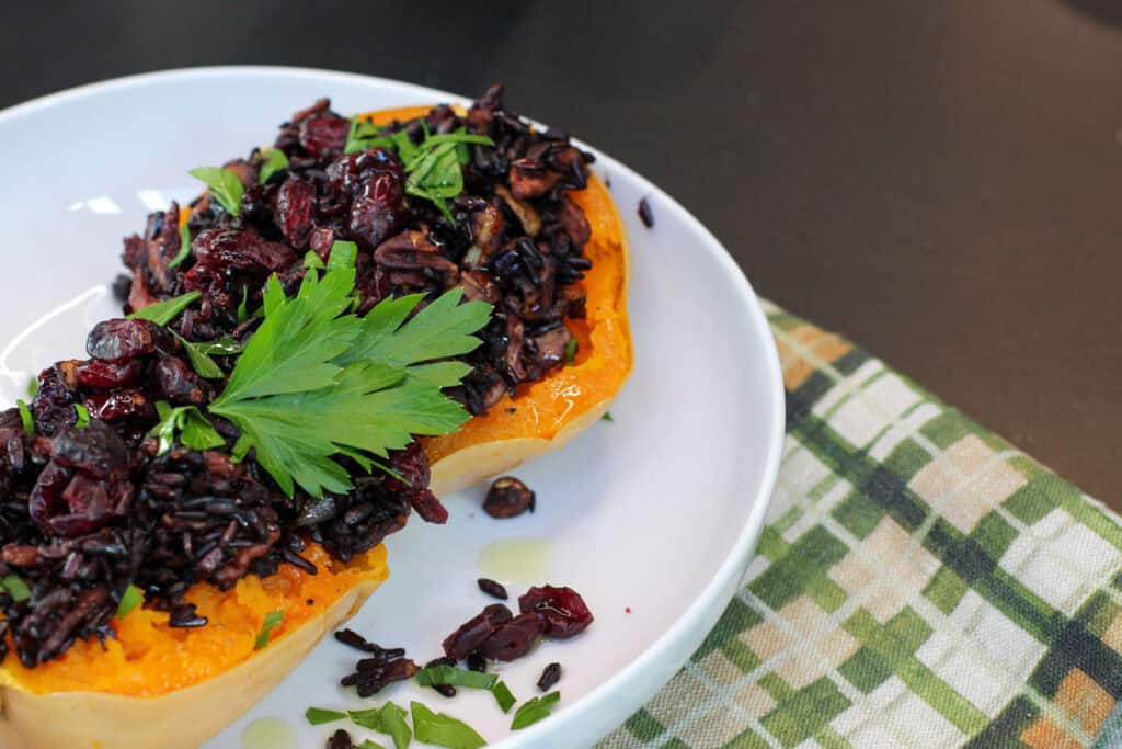 Roasted honeynut squash halves filled with wild rice, mushrooms, cranberries, and toasted pecans, garnished with fresh parsley on a white plate.