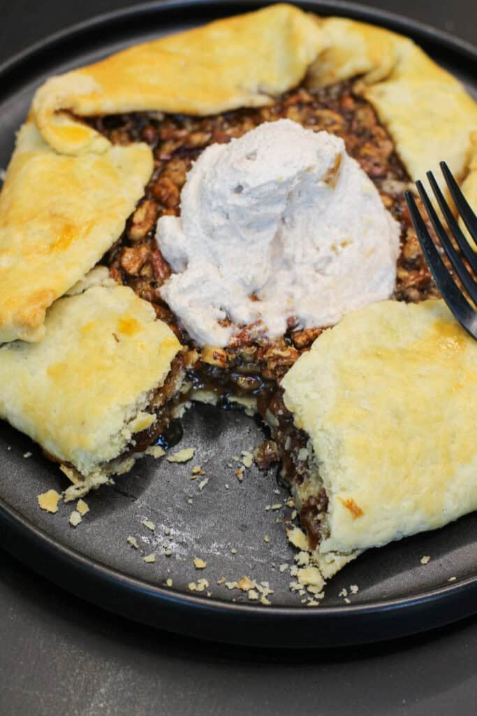 A golden-brown salted maple pecan galette with glossy caramelized filling and flaky folded crust, served with cinnamon whipped cream.