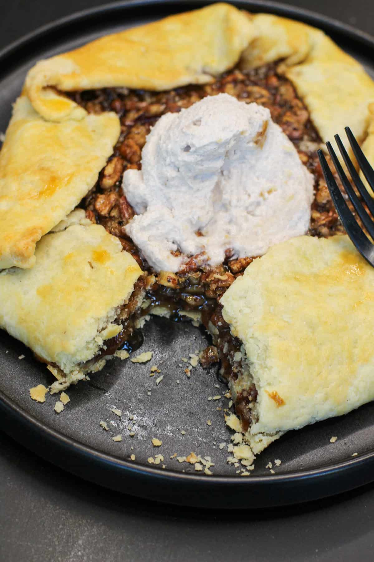 A golden-brown salted maple pecan galette with glossy caramelized filling and flaky folded crust, served with cinnamon whipped cream.