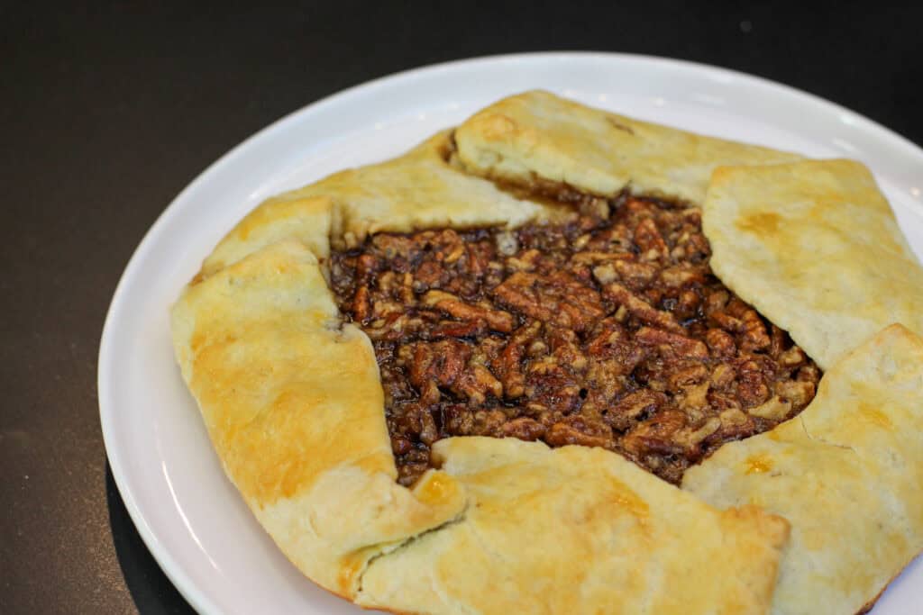 A golden-brown salted maple pecan galette with glossy caramelized filling and flaky folded crust, served with cinnamon whipped cream.