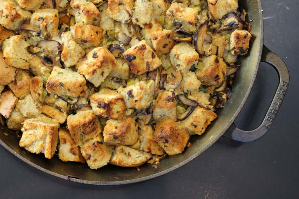 A rustic cast iron skillet filled with wild mushroom and herb sourdough stuffing, topped with crispy edges and a drizzle of garlic olive oil.